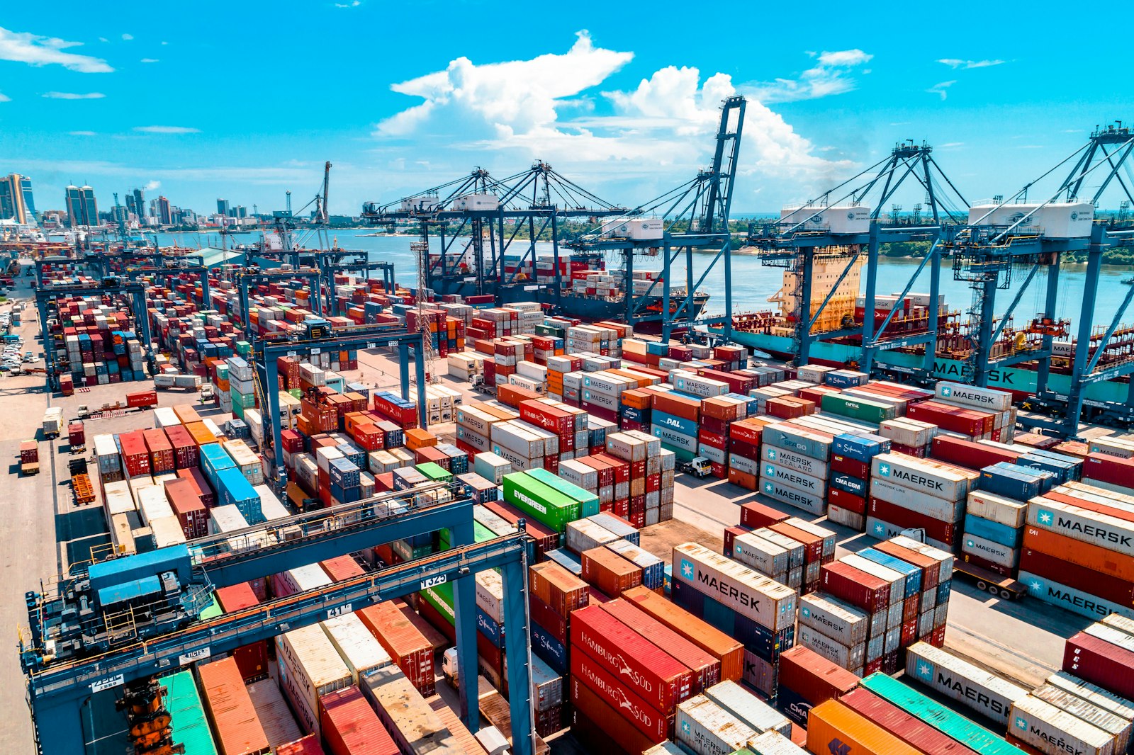 Stacked shipping containers and cranes at a busy container port