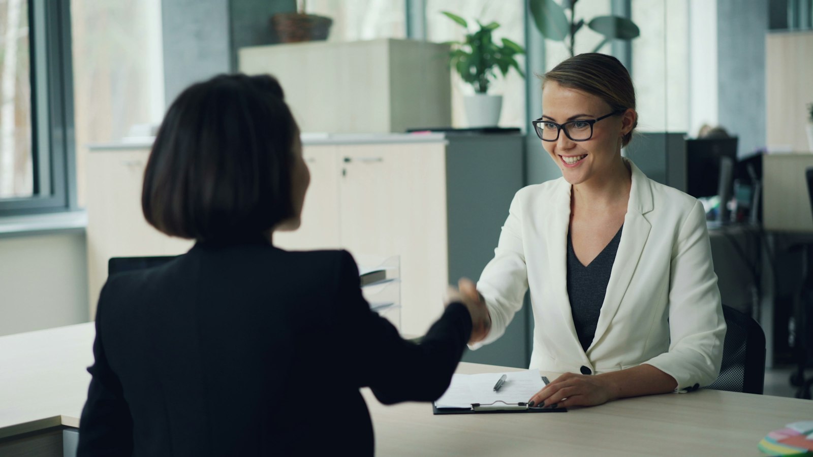 Two professionals shaking hands across a desk after a client meeting